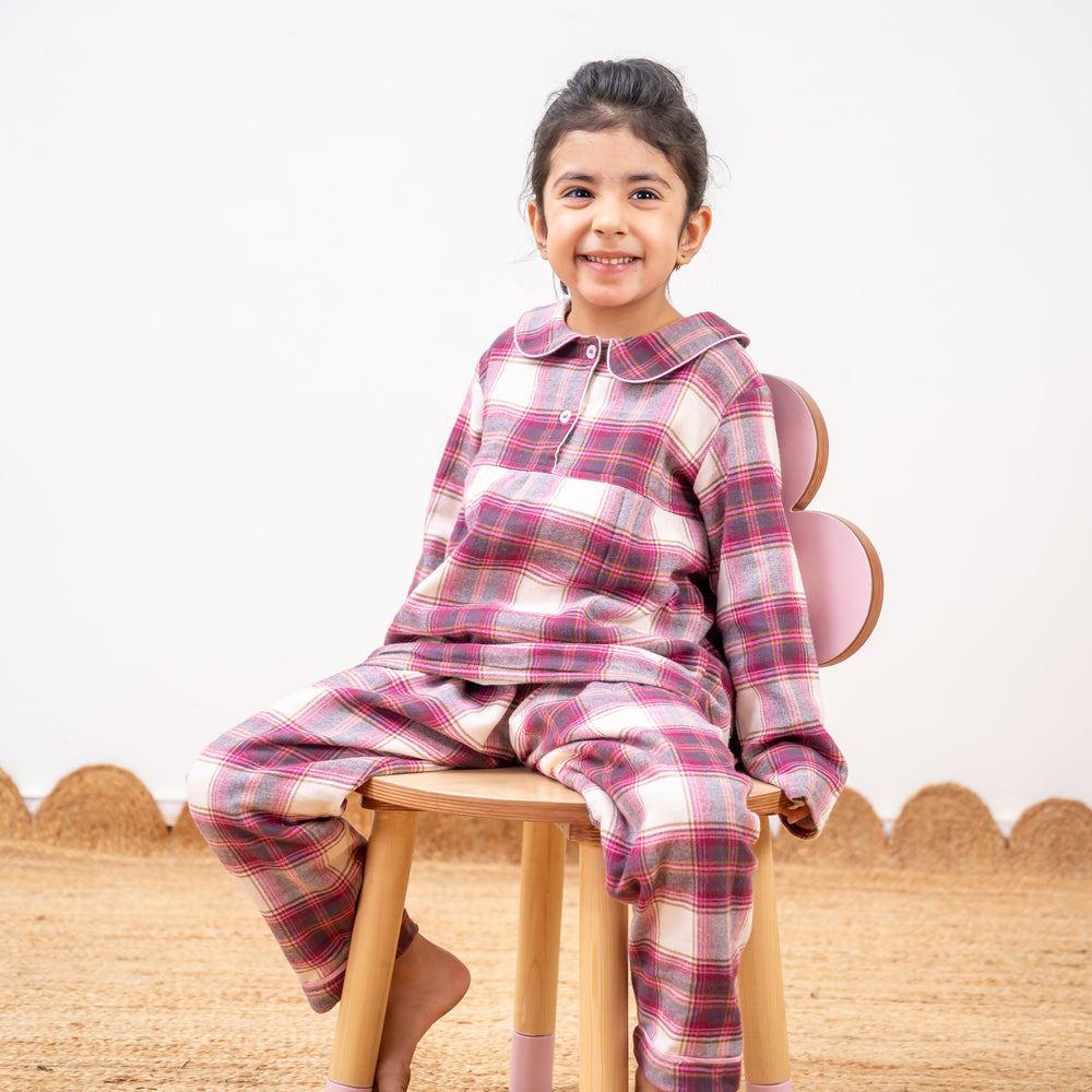 Child wearing a pink plaid outfit sitting on a wooden stool.