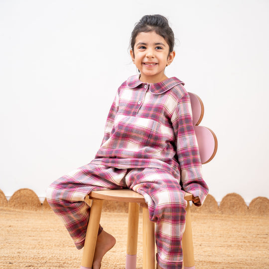Child wearing a pink plaid outfit sitting on a wooden stool.